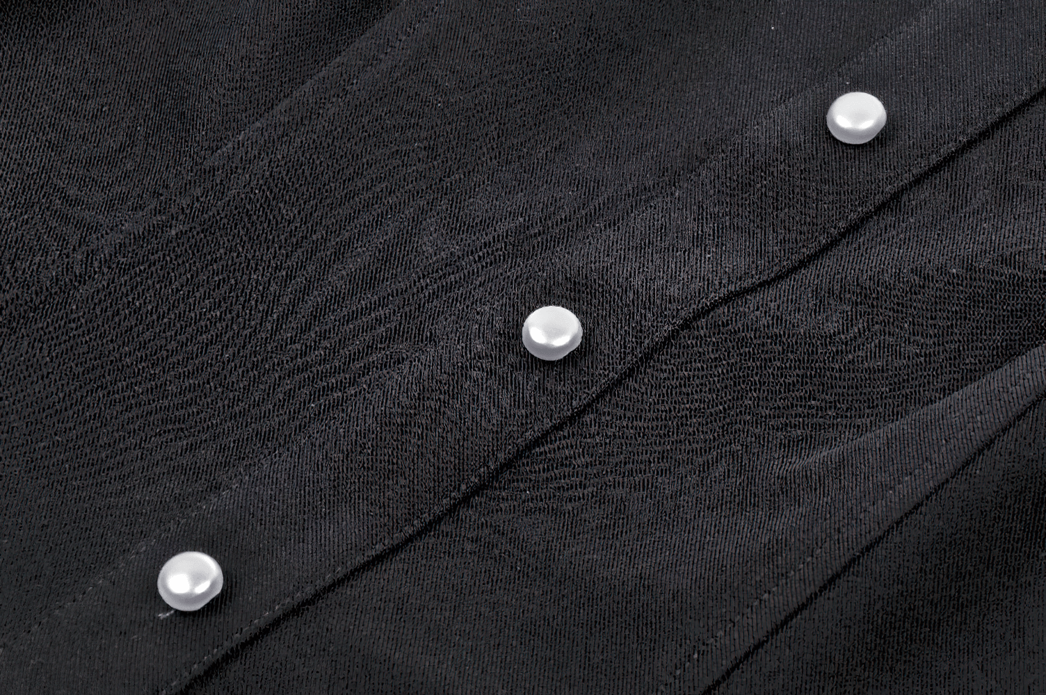 Close-up of black fabric with white pearl buttons, highlighting the elegant details of a vintage blouse.