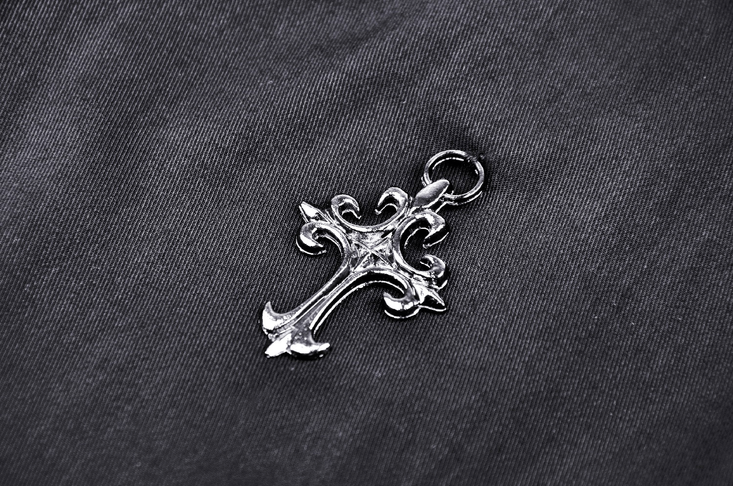 Silver ornate cross pendant resting on a dark fabric background, showcasing intricate details and a charming design.