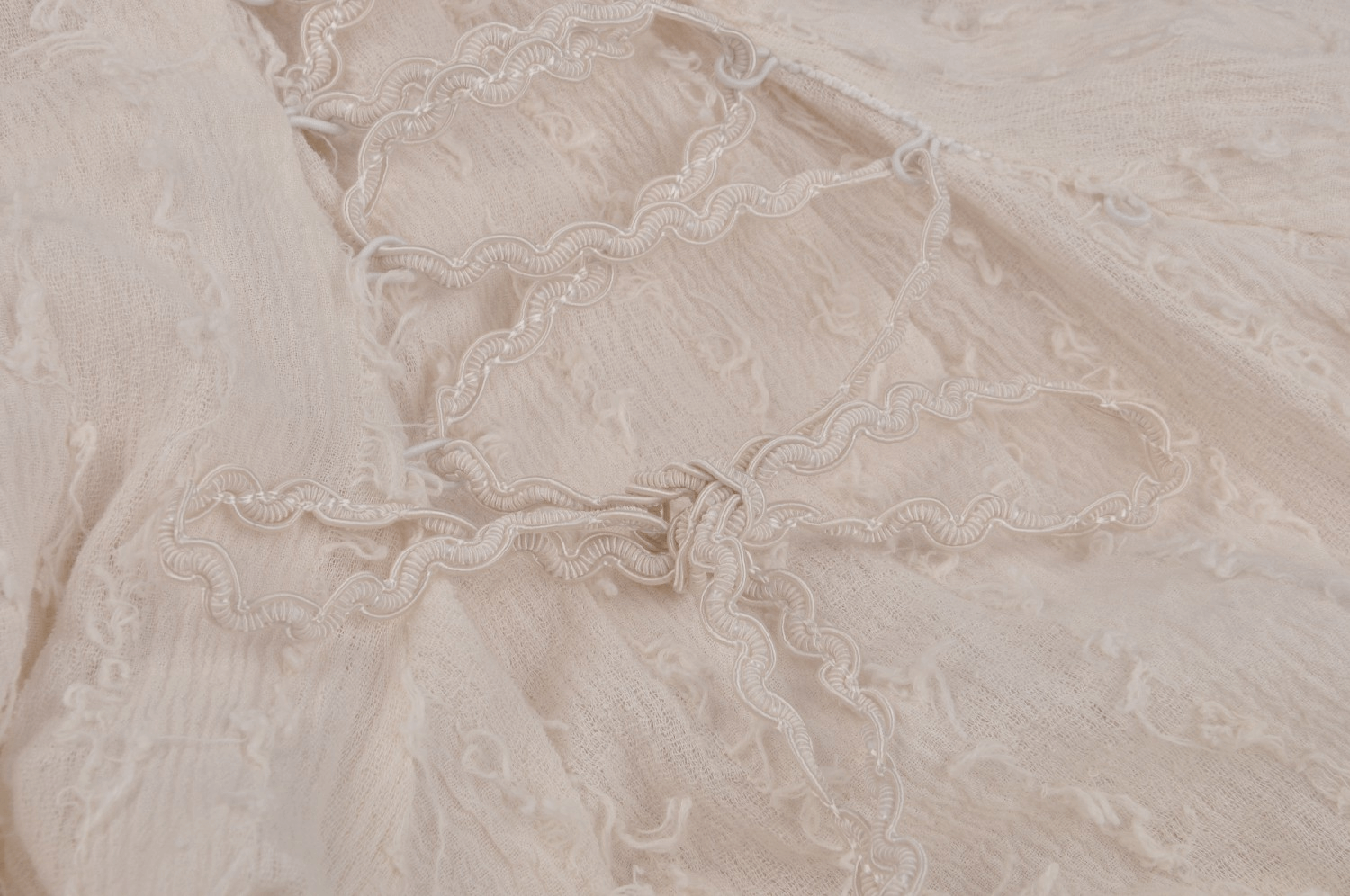 Delicate ivory fabric with intricate lace detail and decorative wavy ribbon tie, perfect for vintage-inspired dresses.