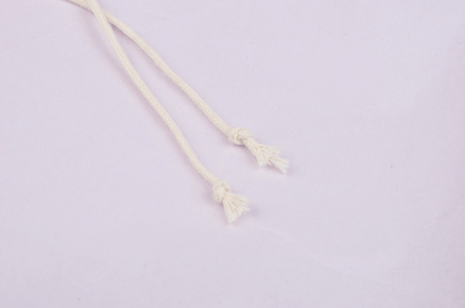 Close-up of two cream-colored drawstring tassels on a light background.
