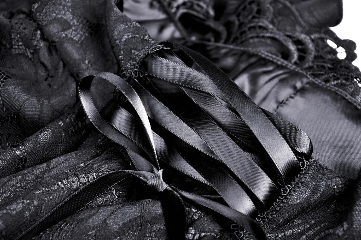 Close-up of black lace fabric with cascading ruffles and satin ribbon tie for a vintage-inspired skirt.