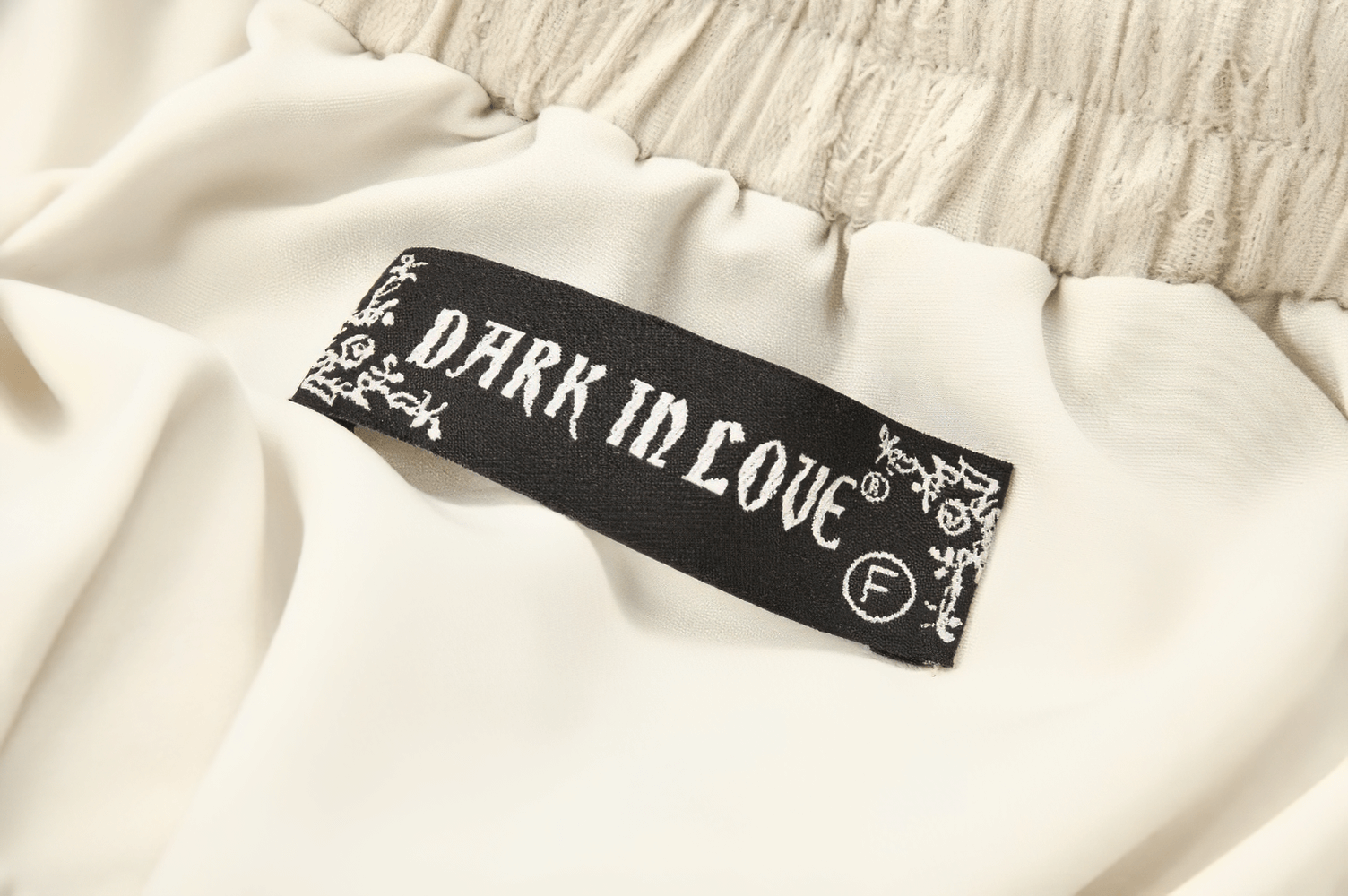 Close-up of 'DARK IN LOVE' clothing label on a cream fabric piece, showcasing brand detail.