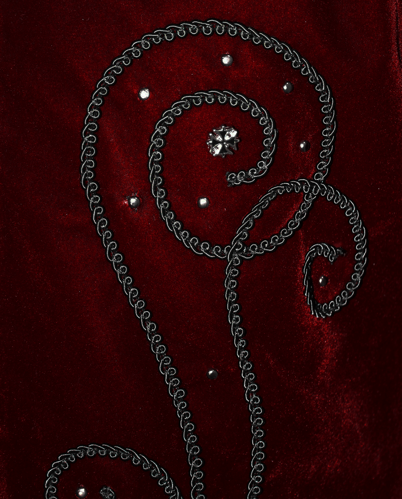 Close-up of intricate black swirl embroidery on wine red velvet, featuring decorative gems and gothic accents.
