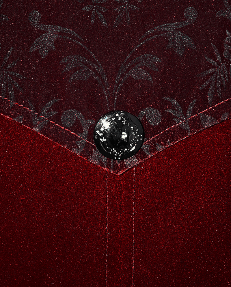 Close-up of vintage men's wine red velvet coat with ornate fabric and decorative button detail.