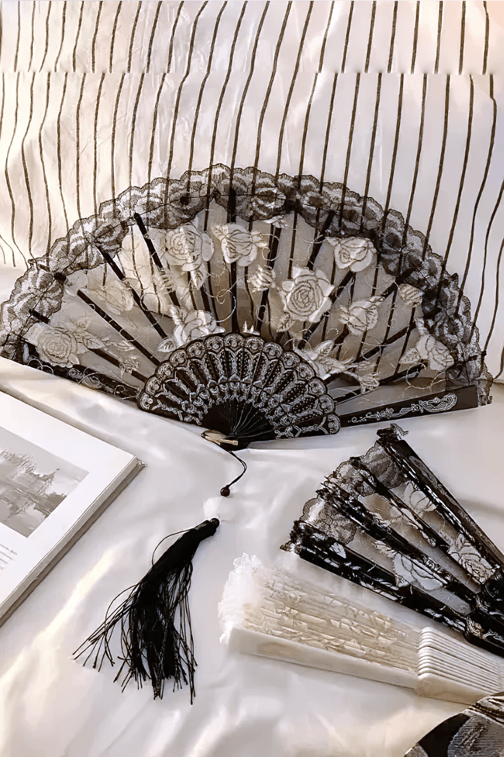 Vintage Rose Lace Folding Fan with Tassel Pendant on a satin surface with decorative tassel and additional fans.