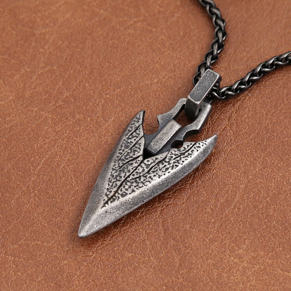 Vintage stainless steel arrowhead pendant necklace on a leather background, stylish unisex fashion amulet.
