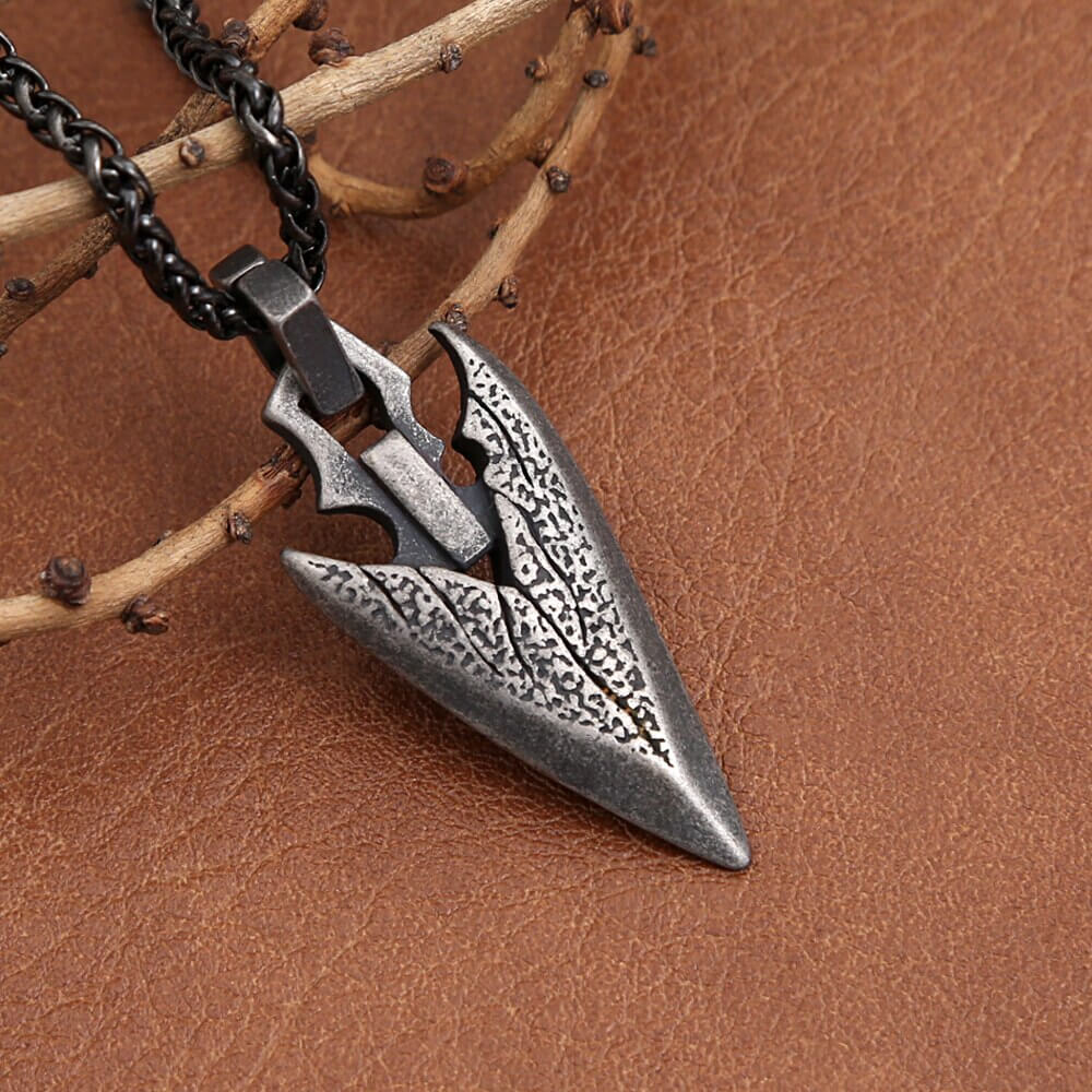 Vintage stainless steel arrowhead pendant necklace on leather background, a stylish unisex fashion amulet accessory.