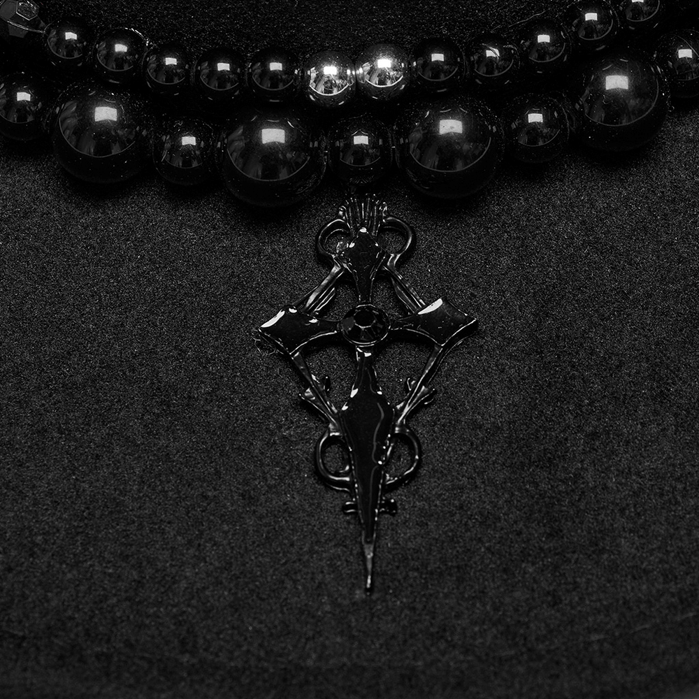 Close-up of the black cross pendant and retro pearl beads on a gothic suede hat. Elegant dark accessory detail.