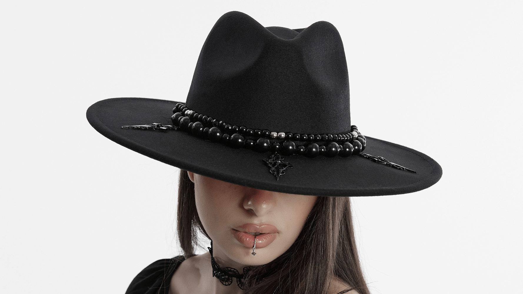 Elegant black wide brim hat adorned with beads and a striking cross, worn by a mysterious model.