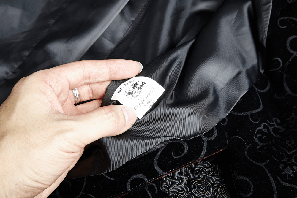 Close-up of a hand holding a care label from a gothic jacket, showcasing luxurious fabric quality.