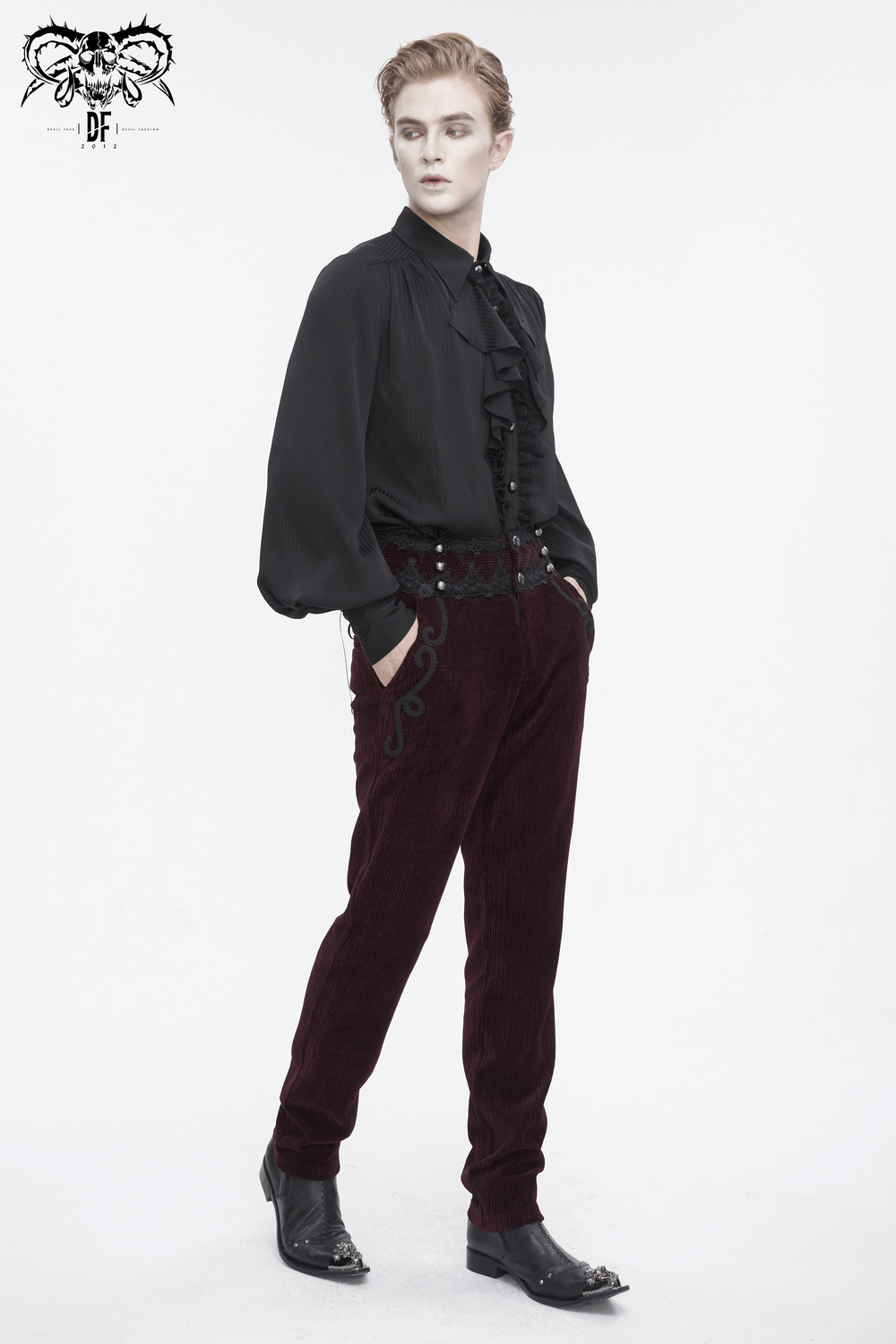 Stylish model in a black ruffled shirt and wine-red lace-trimmed corduroy trousers against a white background.
