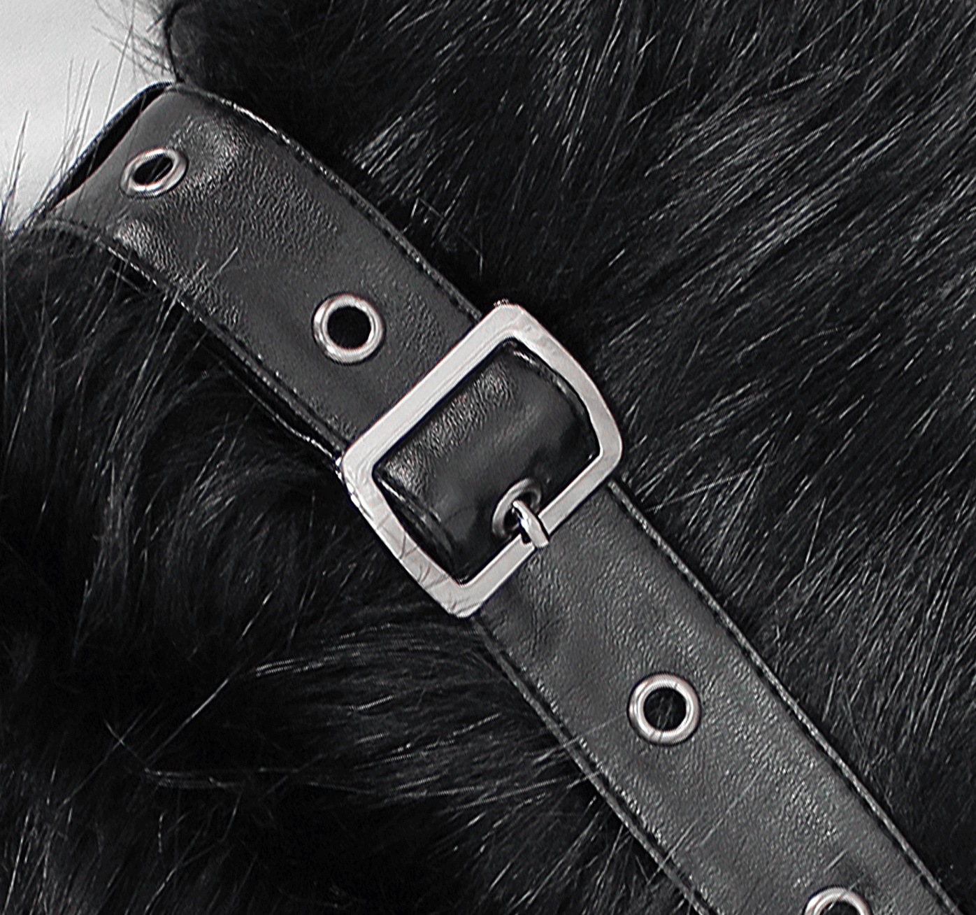 Close-up of a black faux fur coat with a metal buckle and eyelets, highlighting gothic vintage style details.