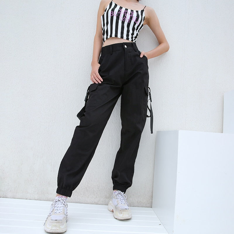 Trendy women wearing black high waist cargo joggers with suspenders, stylishly paired with a striped crop top.
