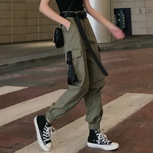 Woman in cargo pants with suspenders, styled in a rock aesthetic, walking on the street with sporty sneakers.