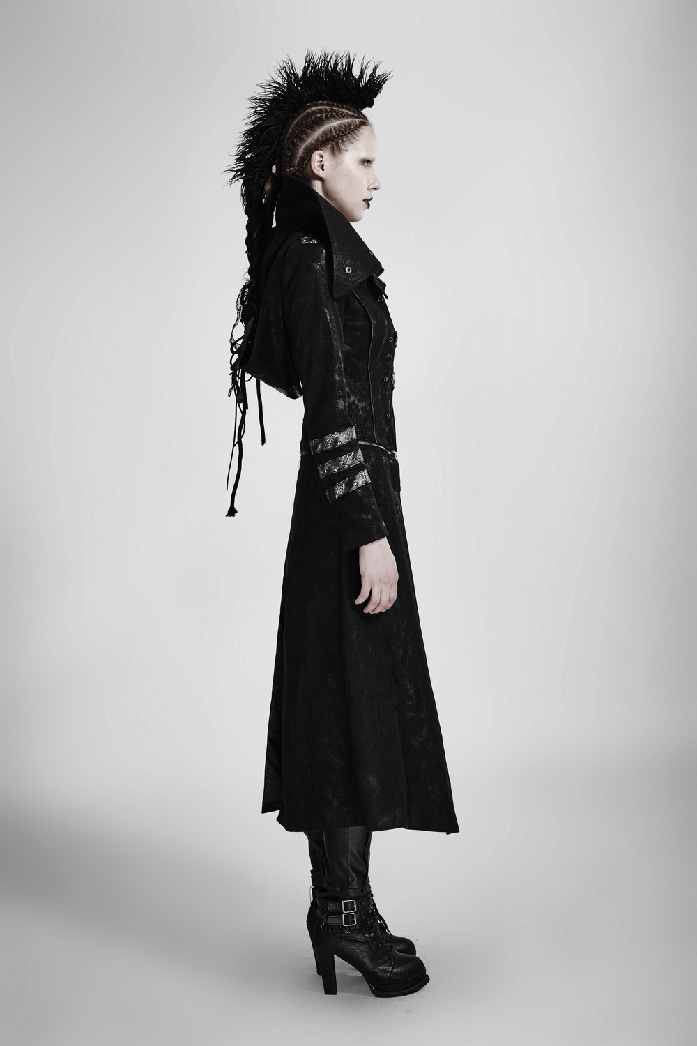 Side view of a woman in a black leather-look long coat with silver accents, showcasing gothic fashion and edgy style.