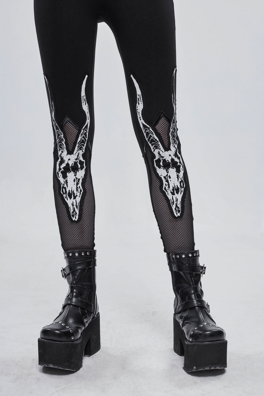 Stylish women's black leggings with white goat skull print and mesh inserts, paired with edgy black platform boots.
