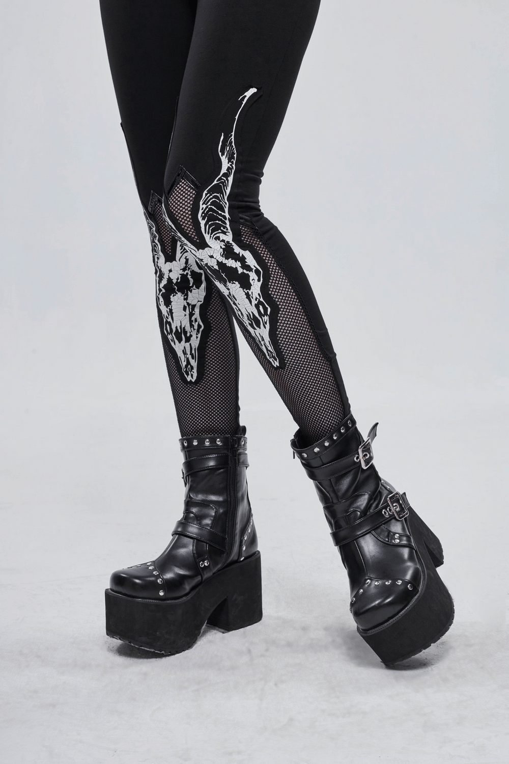 Close-up of women's black leggings with white goat skull print and mesh inserts, paired with stylish black platform boots.