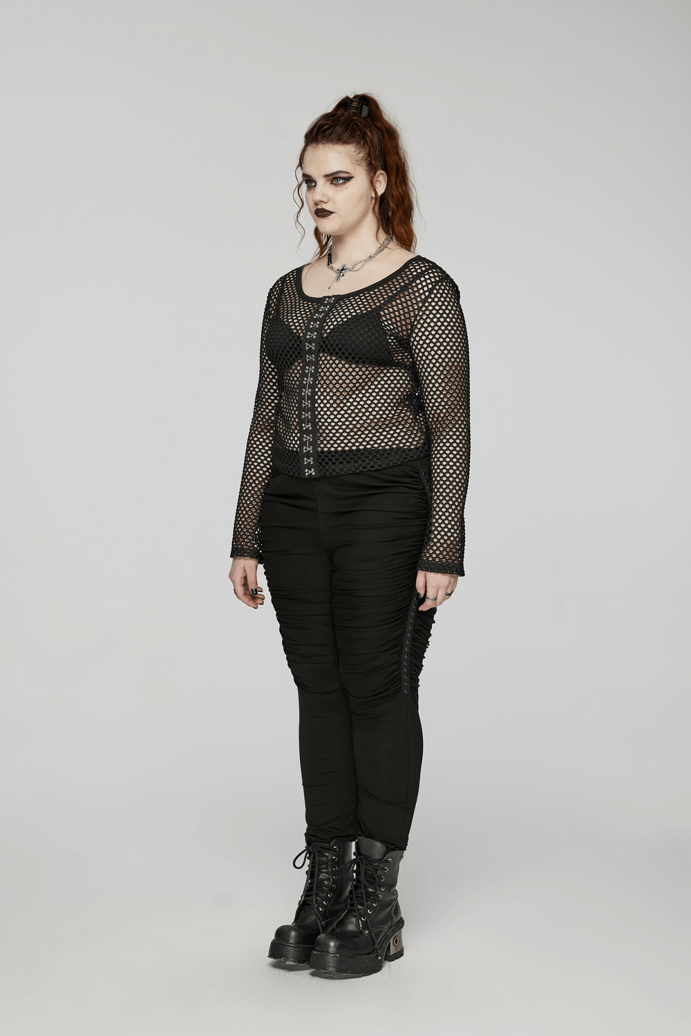 Woman in edgy black mesh long-sleeved top with zip, styled with black pants and combat boots.