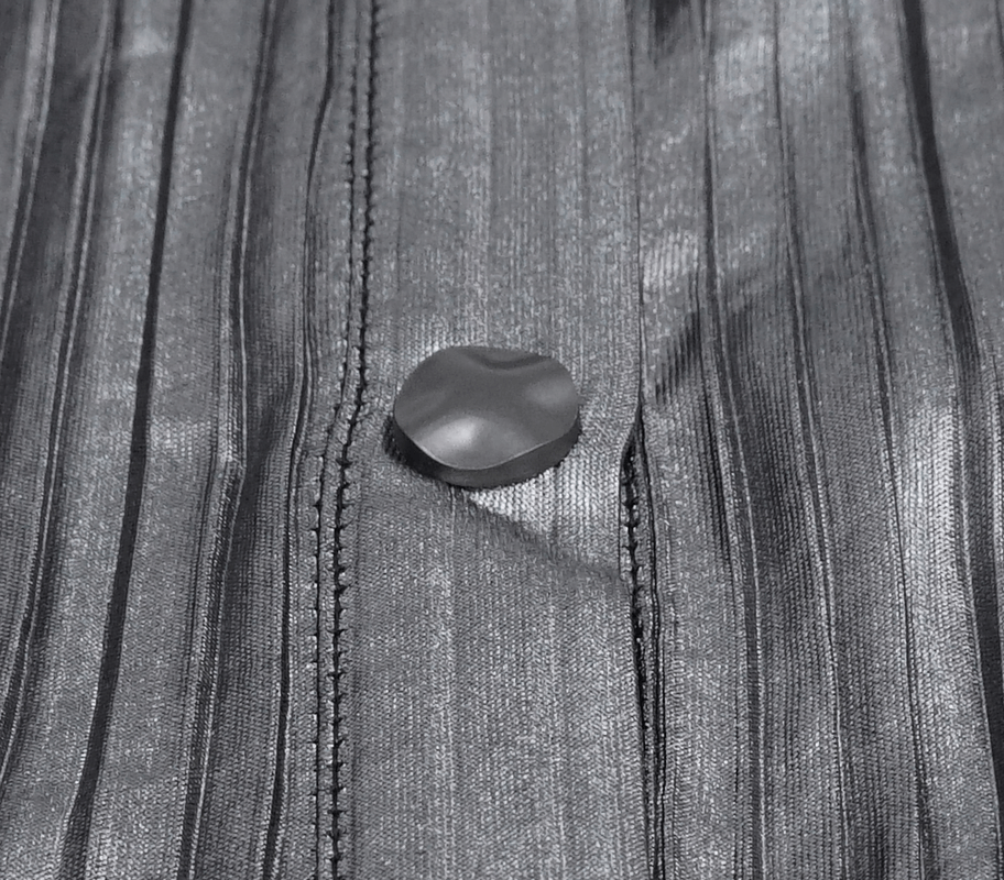 Close-up of a shiny silver blouse featuring a unique button detail on the textured fabric.