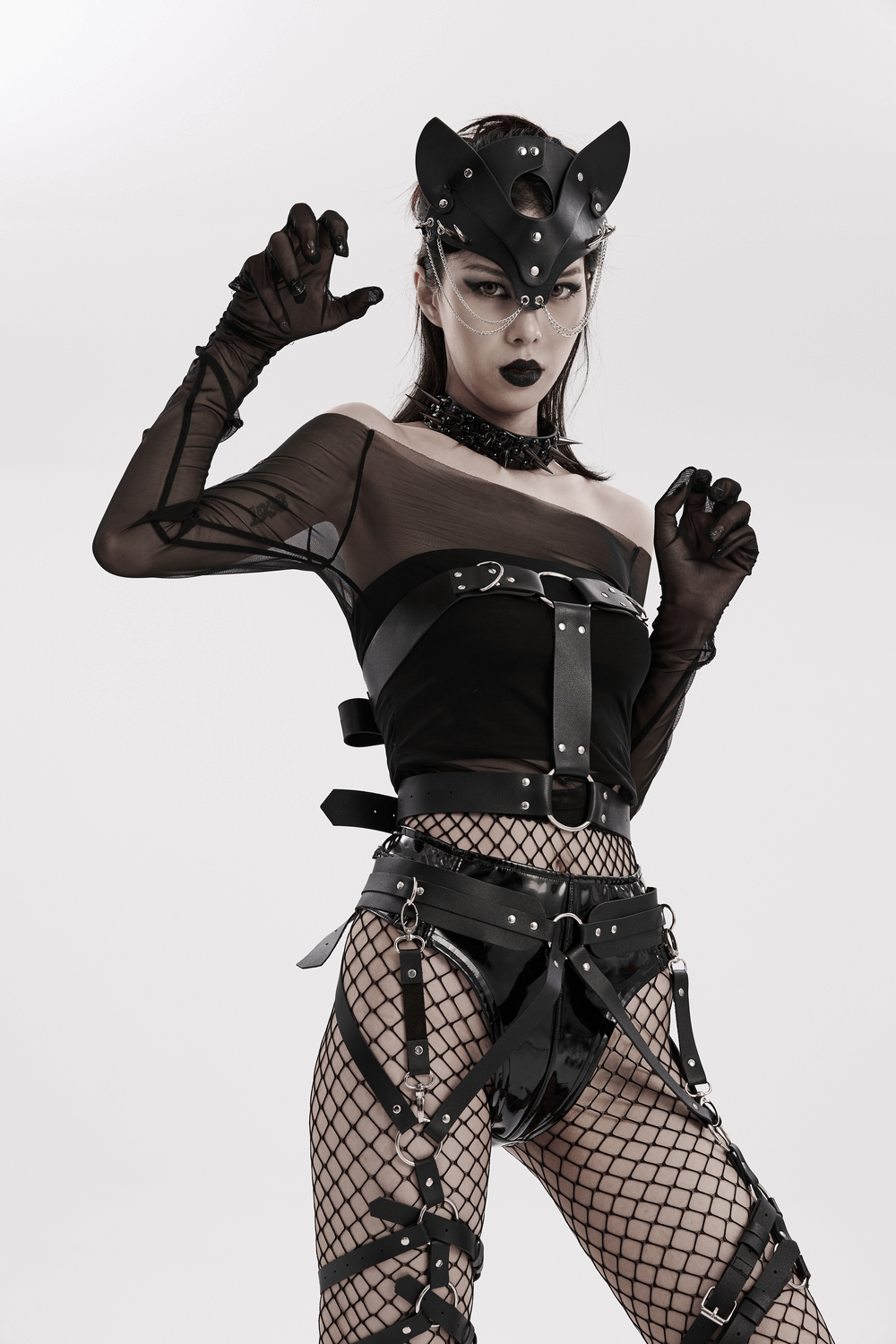 Edgy woman in faux leather gothic strappy harness with mesh sleeves and fishnet stockings, embodying alternative punk fashion.
