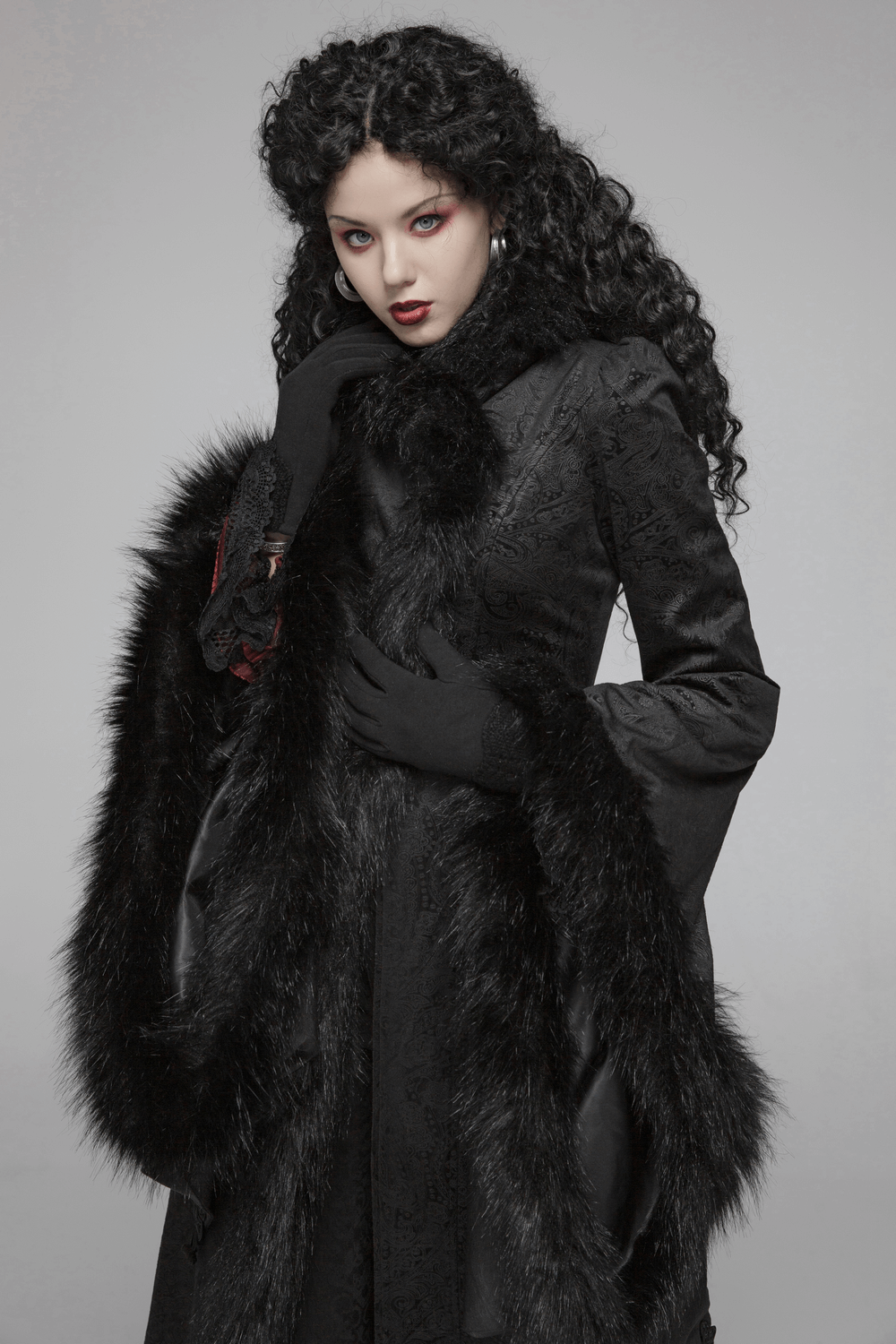 Elegant woman in a gothic long coat with faux fur details and flared sleeves, showcasing a dramatic and refined silhouette.