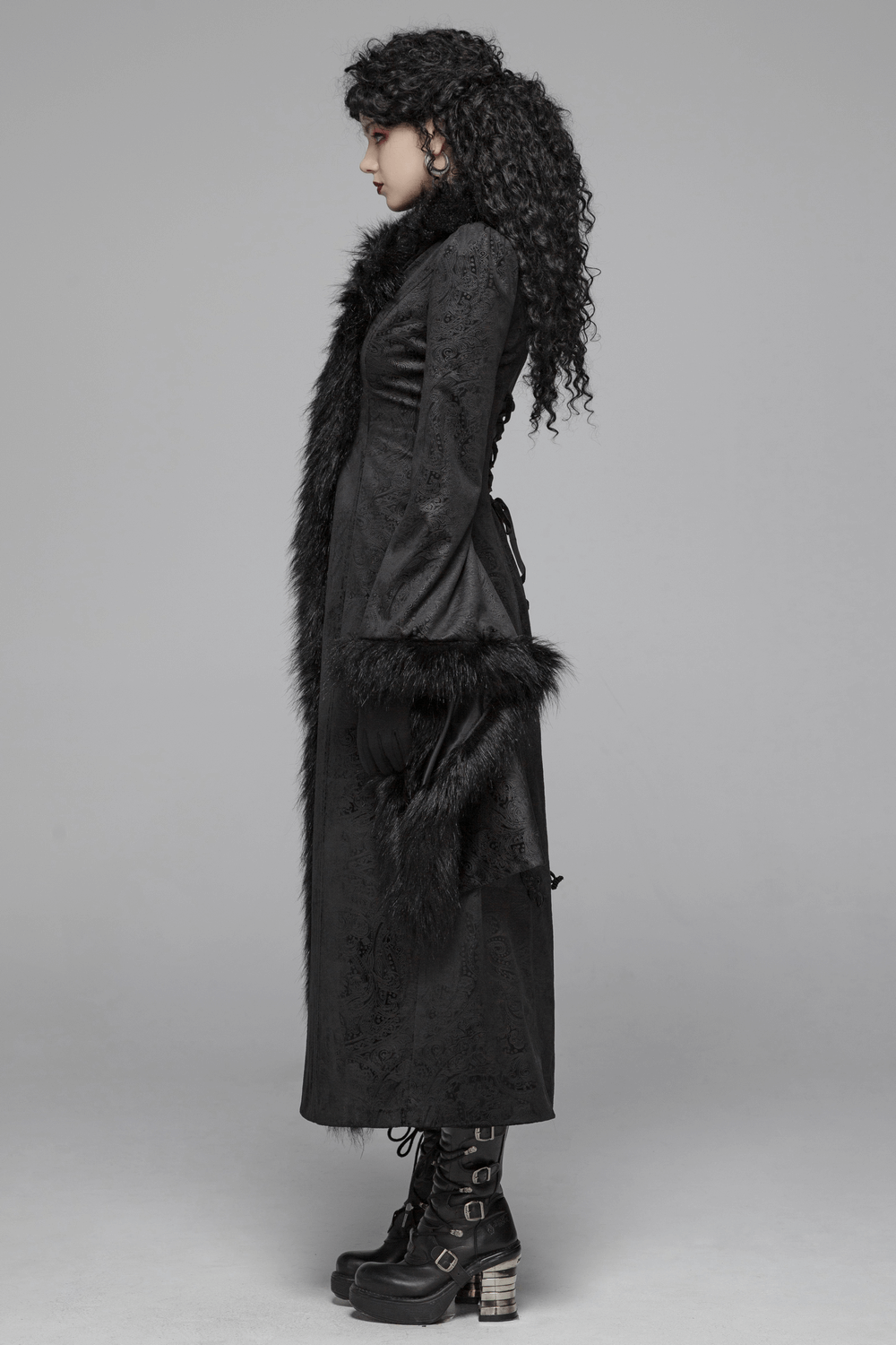 Elegant women's gothic long coat with faux fur trim, flared sleeves, and lace-up back, styled with chic black boots.