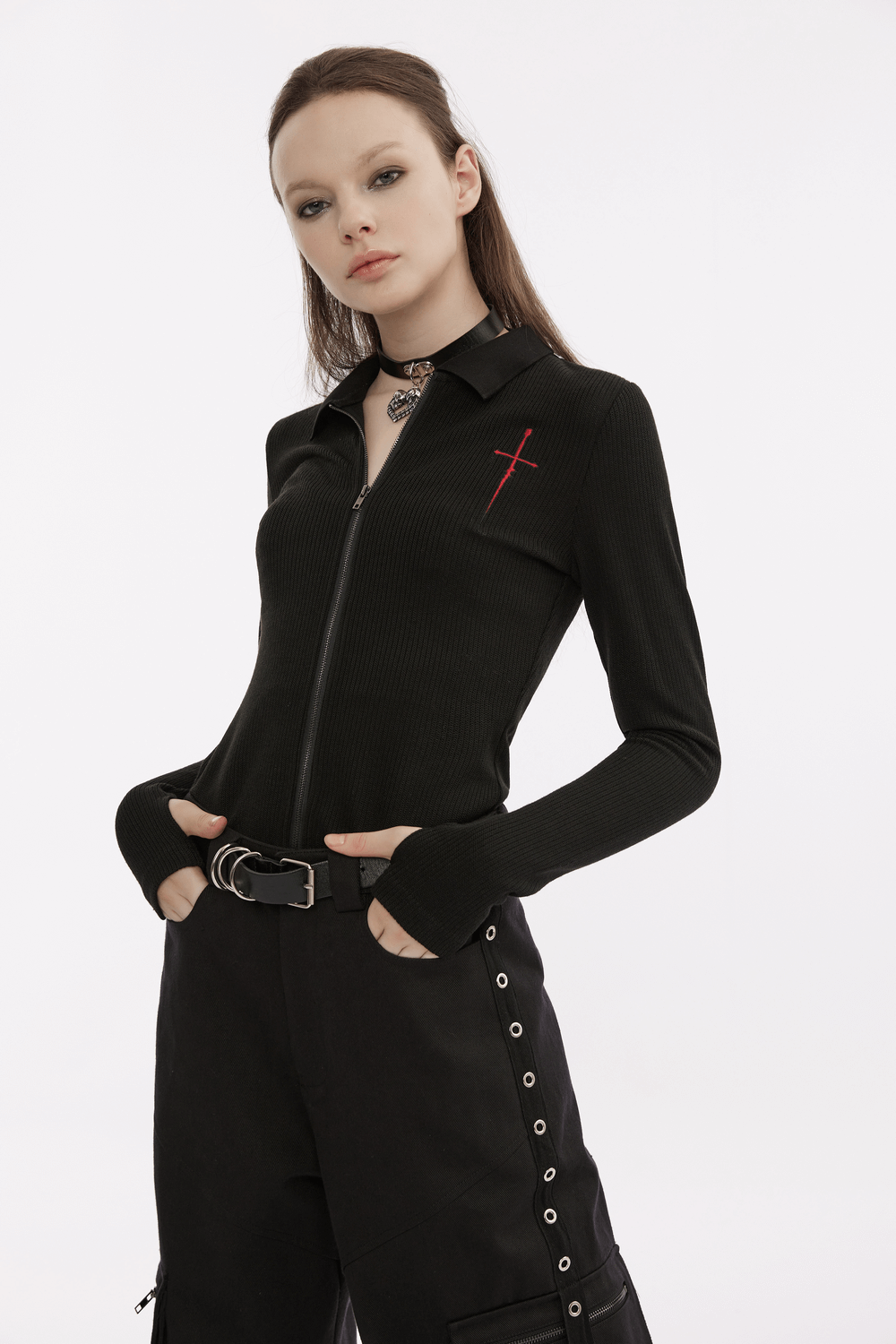 Model wearing a black knitted zippered top with red cross embroidery, paired with edgy black pants.