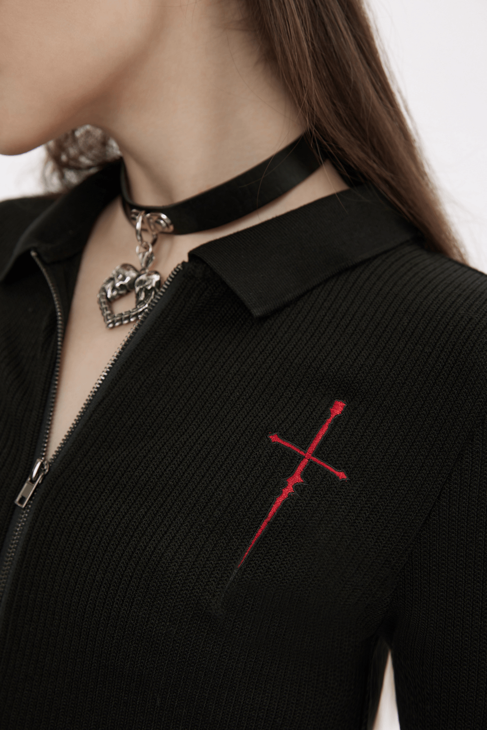 Close-up of women's black knitted top featuring red cross embroidery and zip detail, styled with a choker necklace.