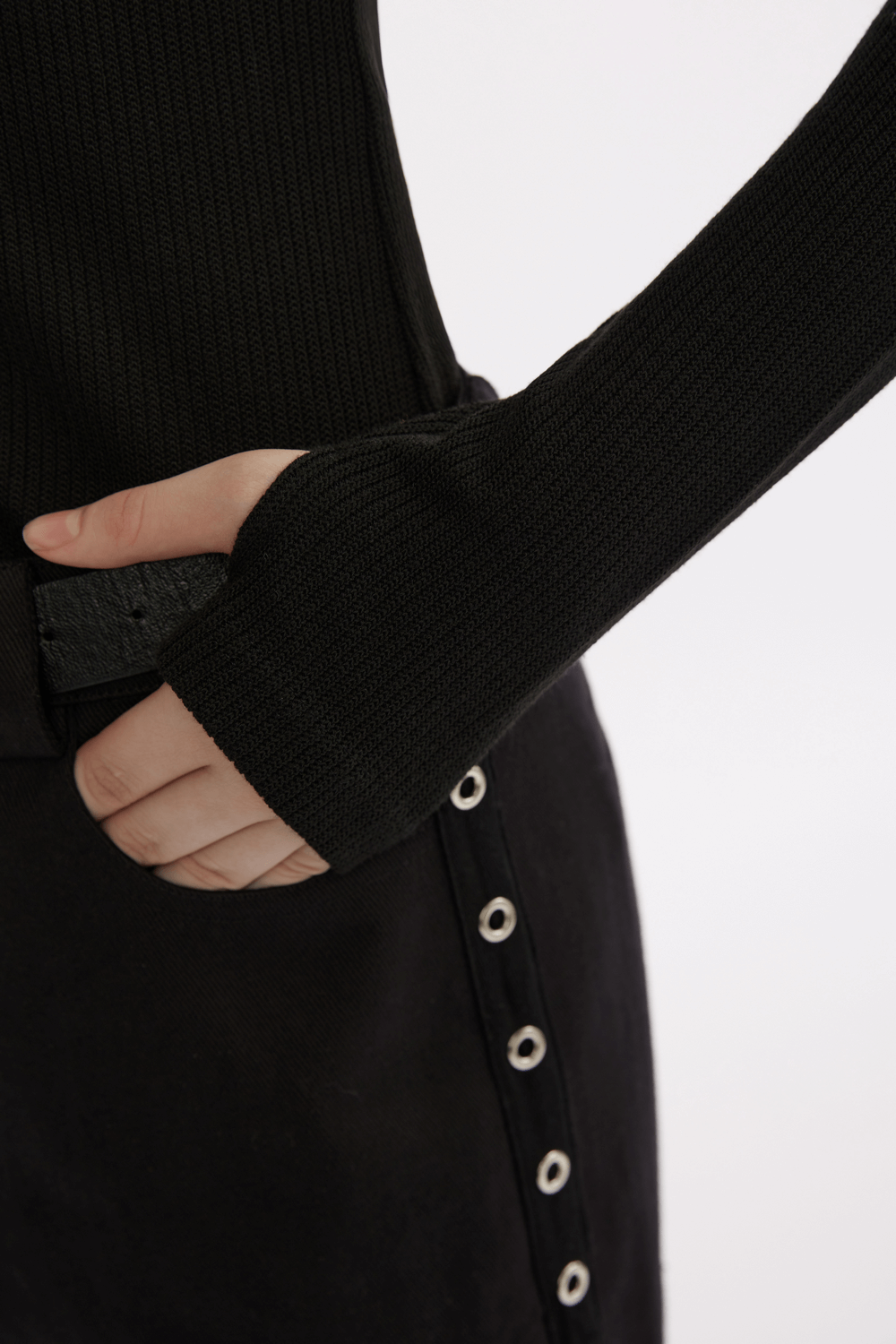 Close-up of a woman's hand in a black knitted top with extended sleeves, showcasing stylish ribbed texture.