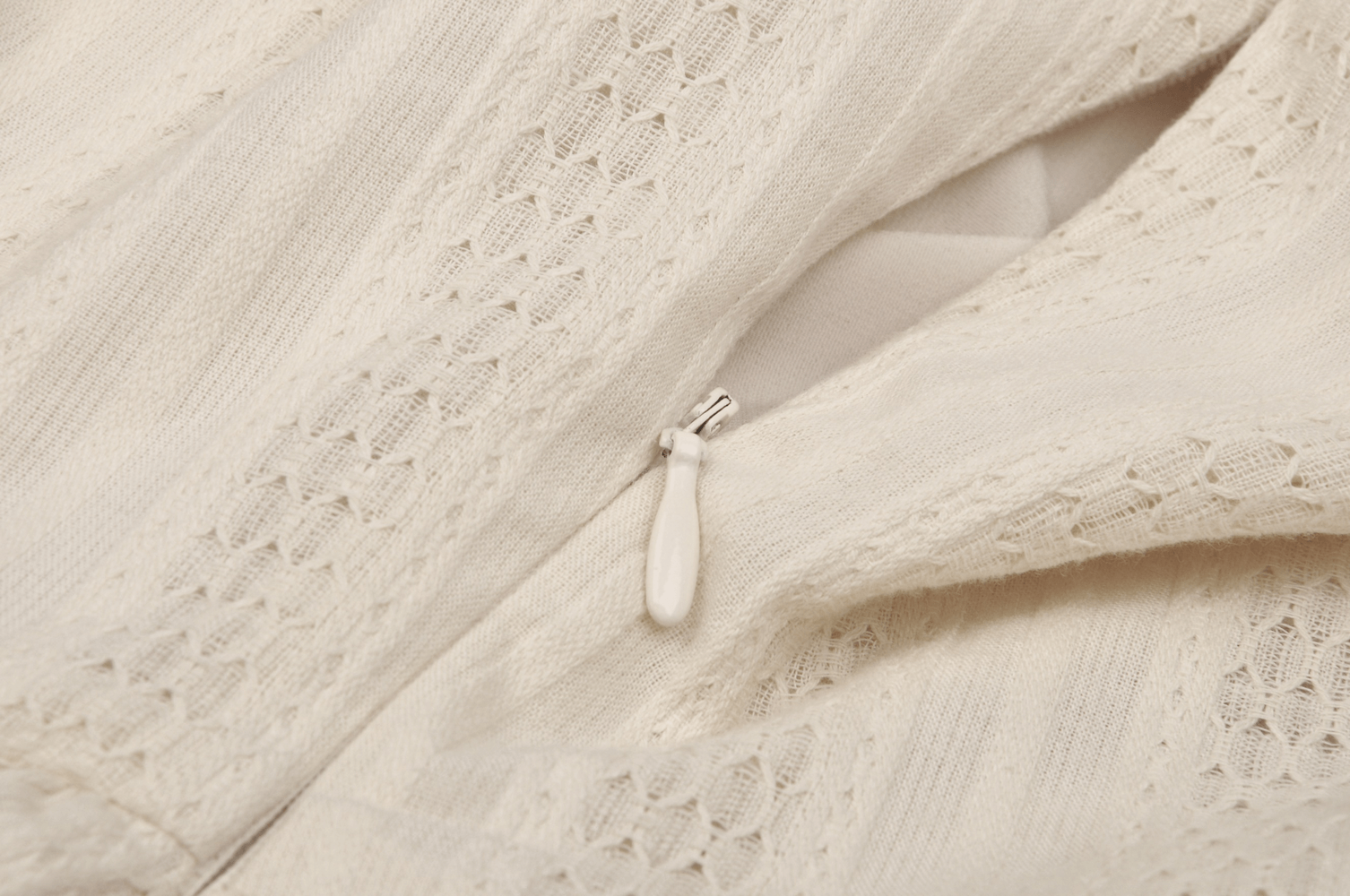 Close-up of off-white lace fabric with a zipper detail, showcasing intricate texture for a feminine mini dress.