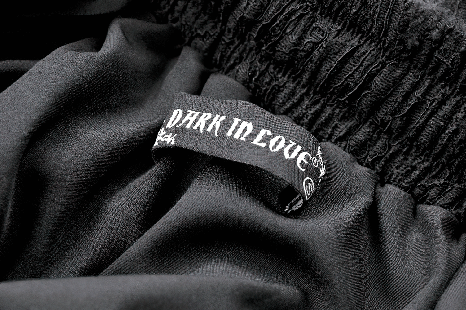 Close-up of the 'Dark in Love' label on a black fabric, showcasing gothic fashion style and intricate details.