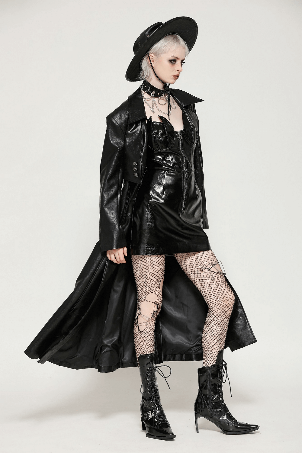 Fashion model wearing women's long black faux leather trench coat with belt and dress, paired with hat and boots.