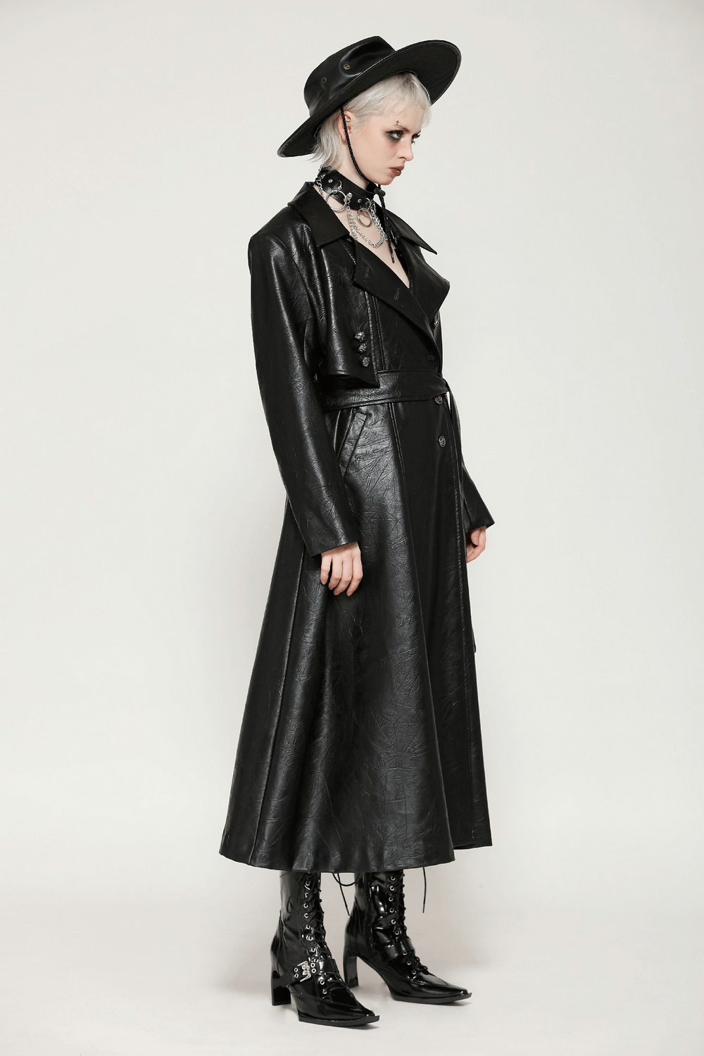 Stylish woman in a full-length black faux leather trench coat with belt and wide-brimmed hat, showcasing edgy fashion.