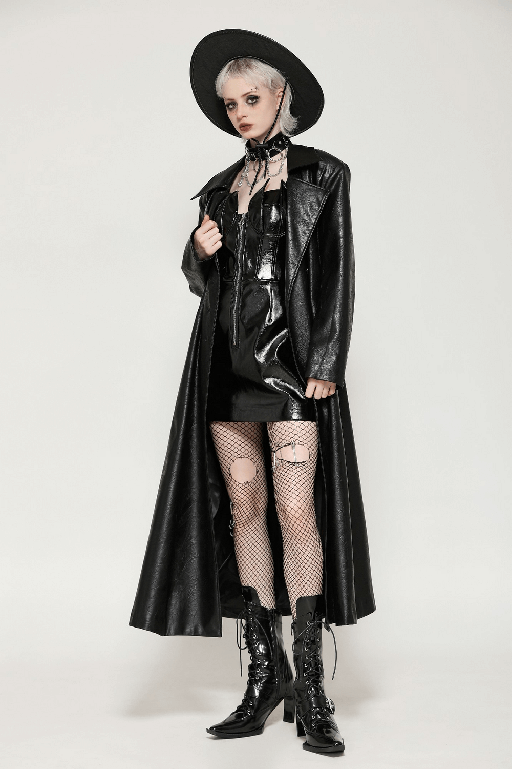 Stylish model in a long black faux leather trench coat with a wide-brim hat and fishnet stockings, exuding edgy elegance.