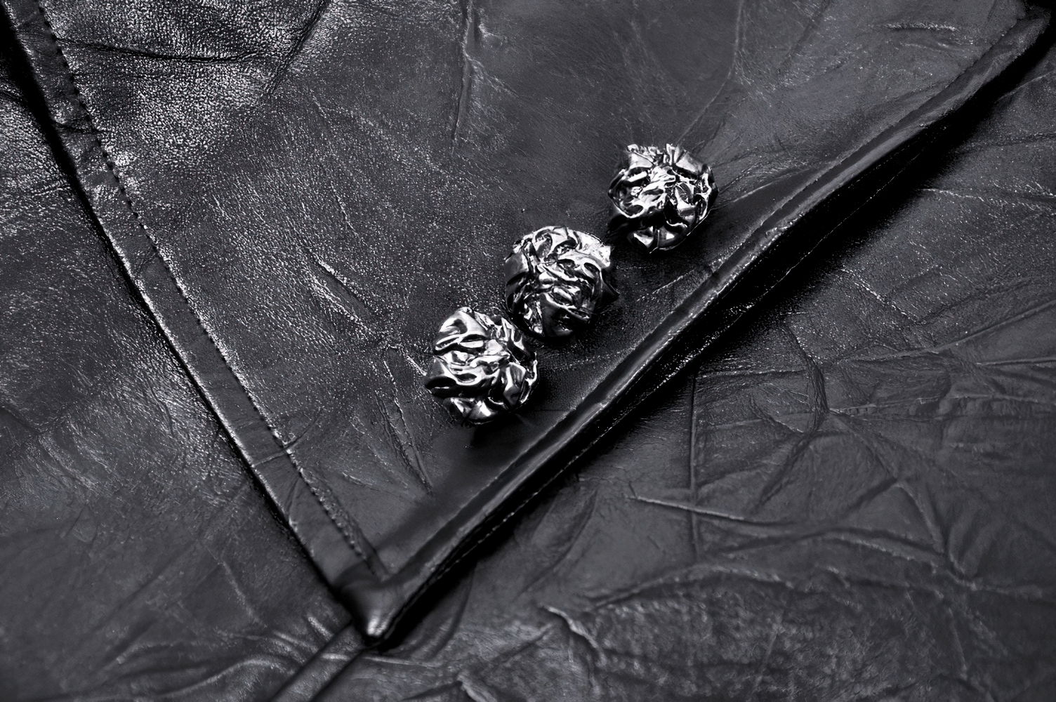 Close-up of black faux leather fabric with three decorative metal buttons.