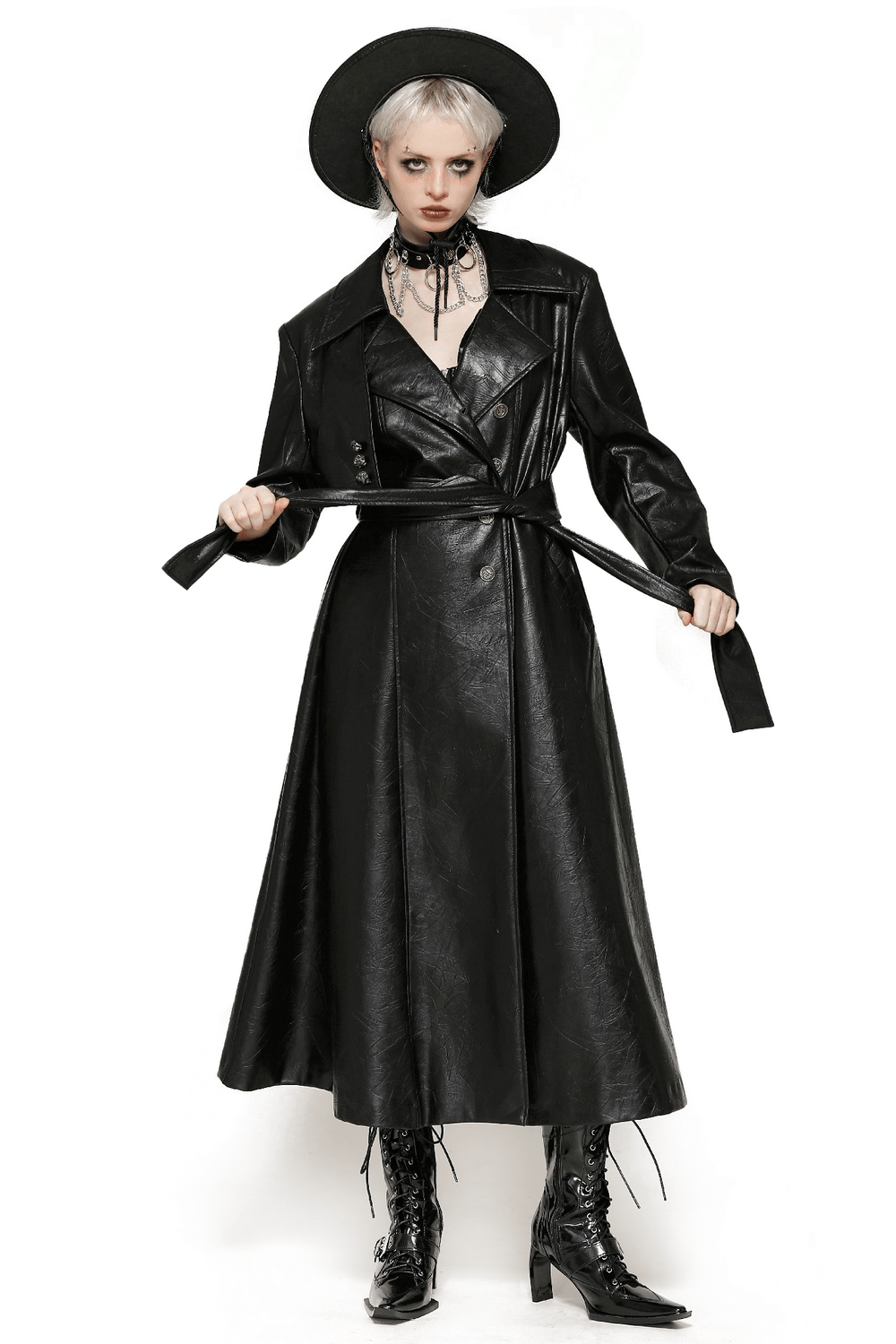 Woman in long black faux leather trench coat with belt and hat, showcasing bold and edgy style with double-breasted design.