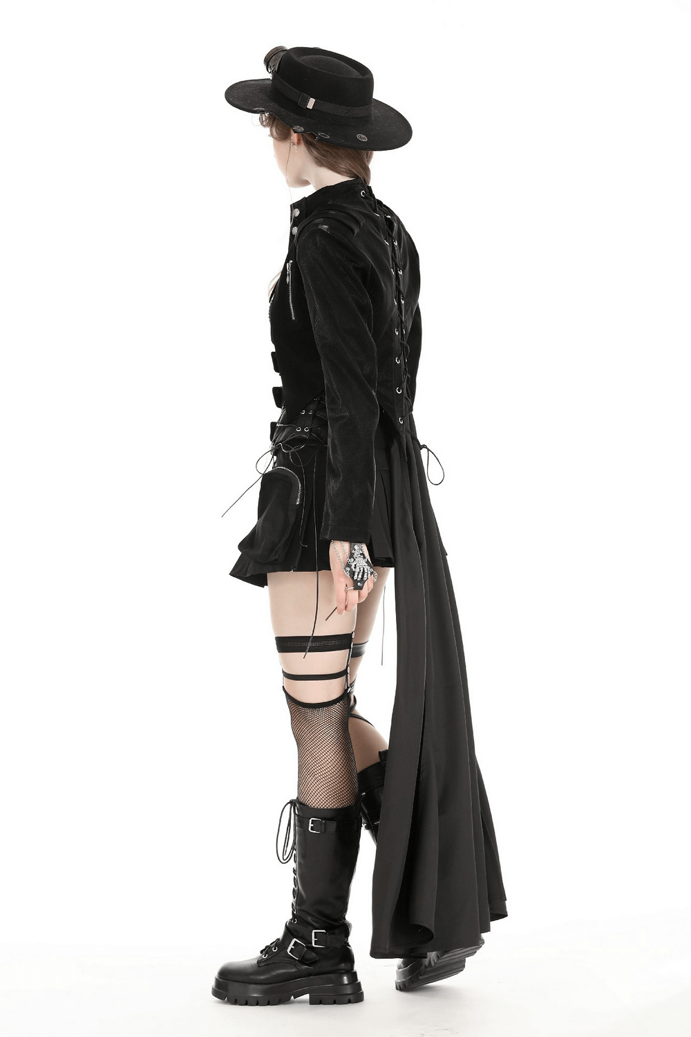 Woman in gothic black cape with laces, stylish hat, and chunky boots, showcasing a bold fashion statement.