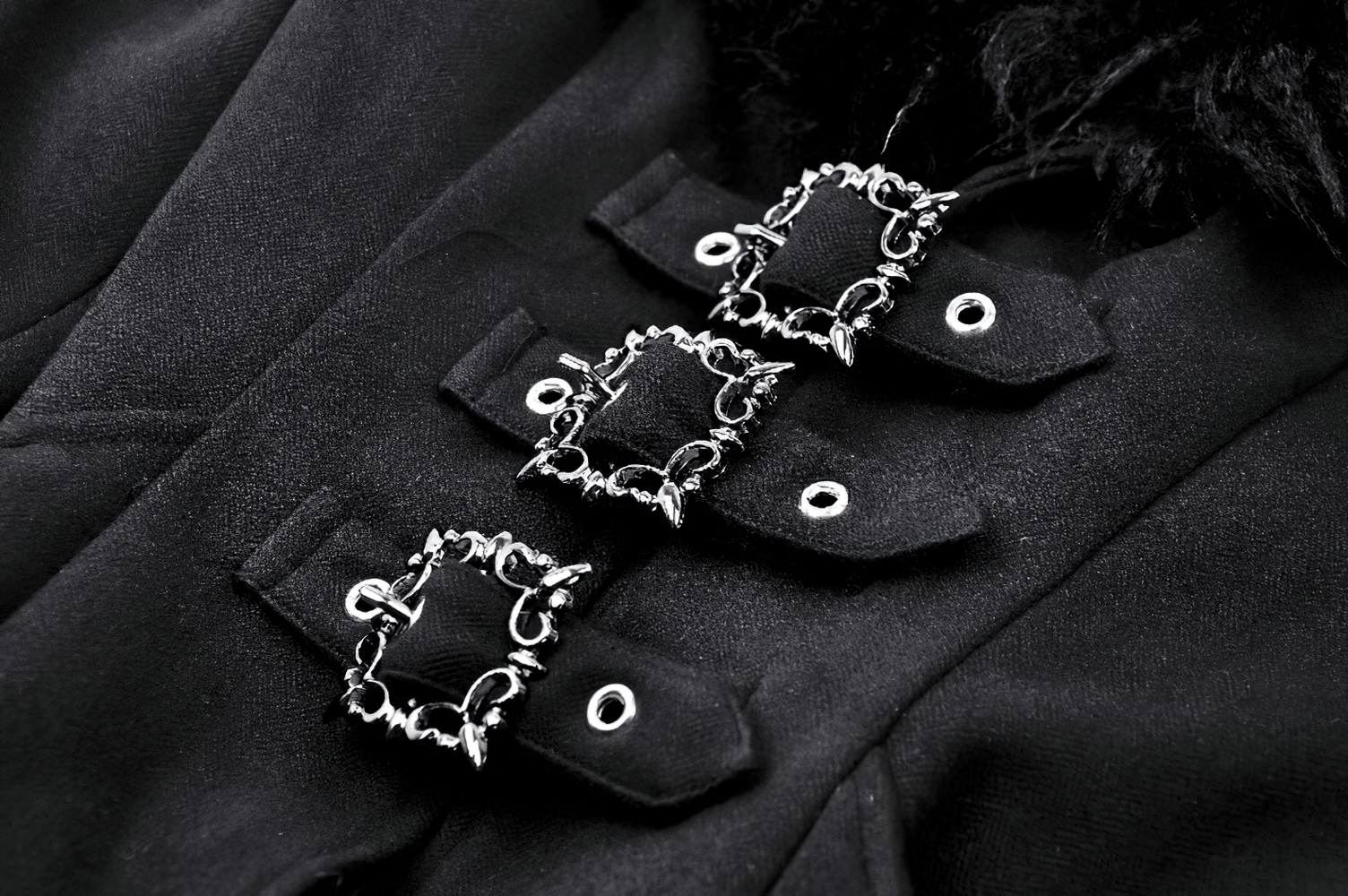 Close-up of decorative silver buckles on a black trench coat with faux fur trim.