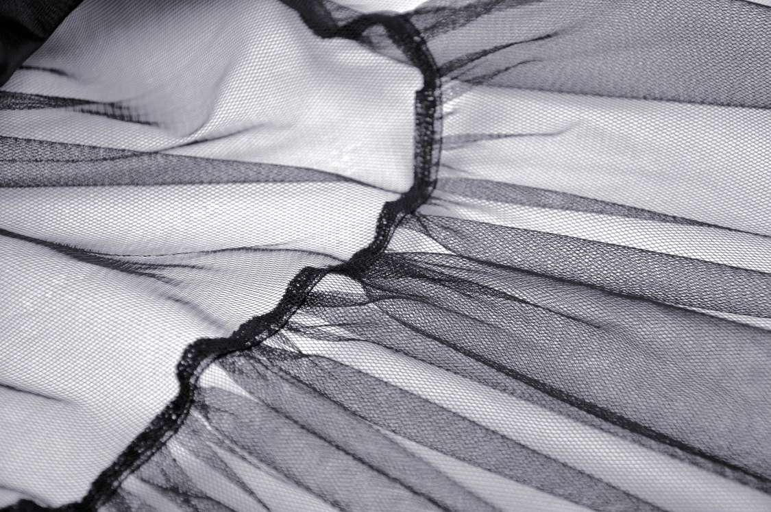 Close-up of black lace and mesh fabric with ruffles, showcasing gothic elegance in a high-low skirt.