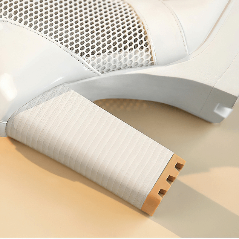 Close-up of a stylish white patent leather high heel with a mesh design and textured heel.