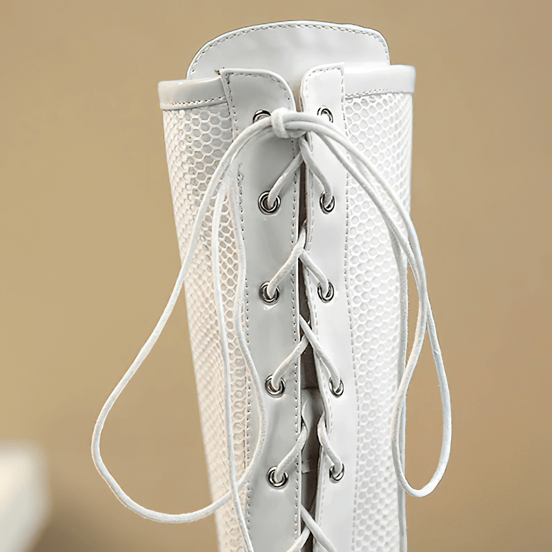 Close-up of women's patent leather knee-high boots with intricate mesh details and stylish lace-up design.