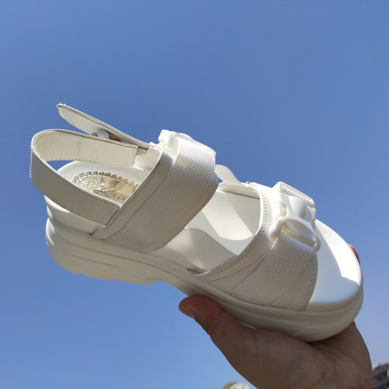 White women's platform sandals with adjustable straps and chunky rubber sole against a clear blue sky.