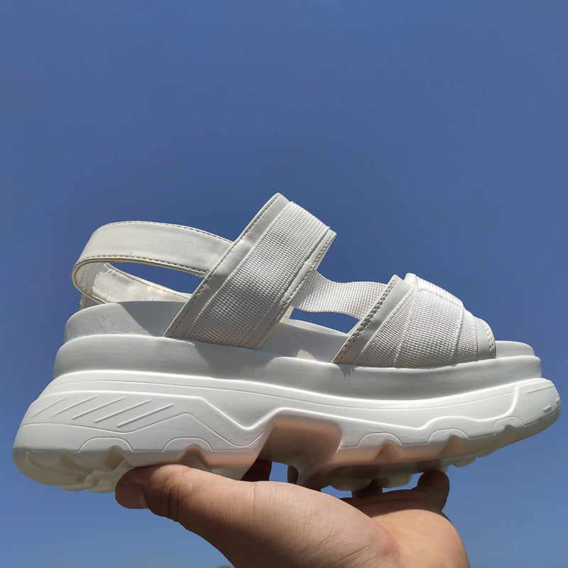 White women's platform sandals with adjustable straps and thick rubber sole against a clear sky.