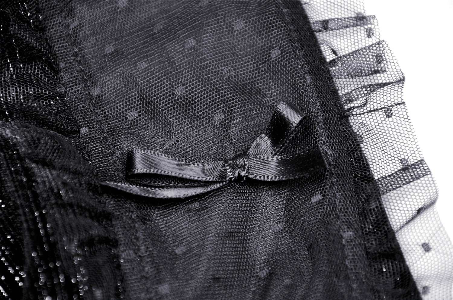 Close-up of sheer black fabric with polka dots and a satin bow detail, perfect for vintage-inspired designs.