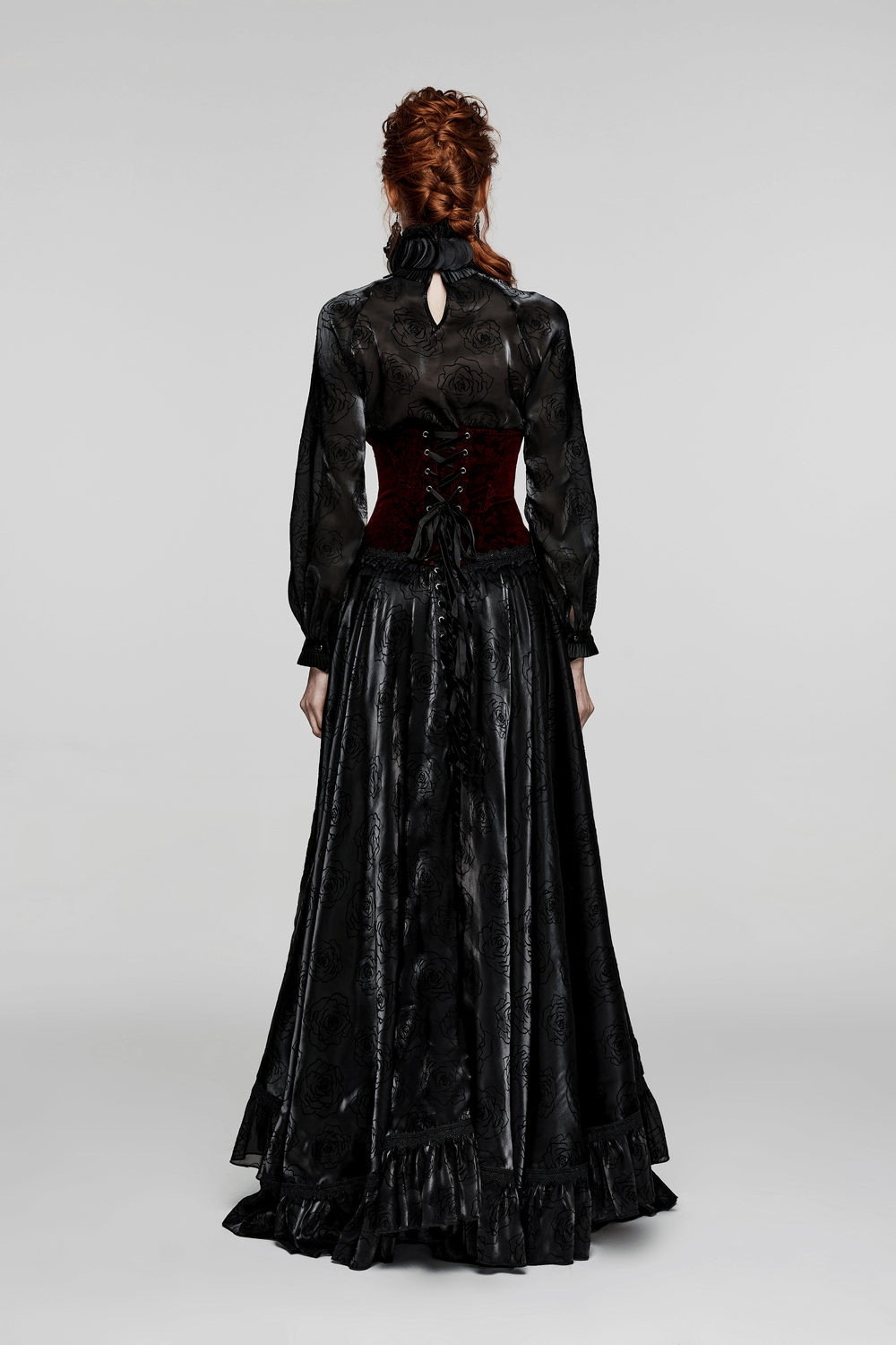 Back view of a woman in a long black gothic dress with a velvet corset featuring lace accents and a tie-back.