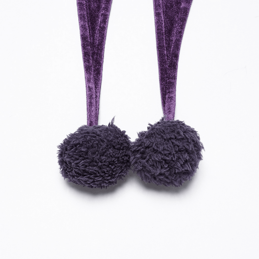 Close-up of fluffy fur ball ties on a purple velvet hooded cape for a whimsical touch.