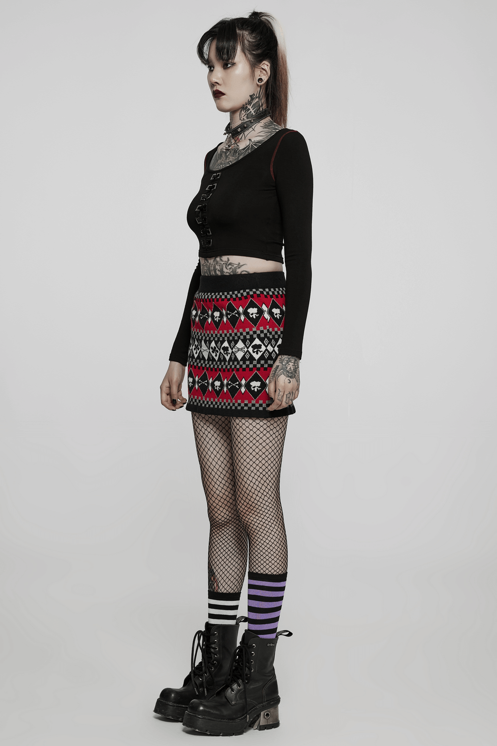 Model showcasing a wool-blend knit skirt with geometric skull design, paired with a stylish black top and fishnet stockings.