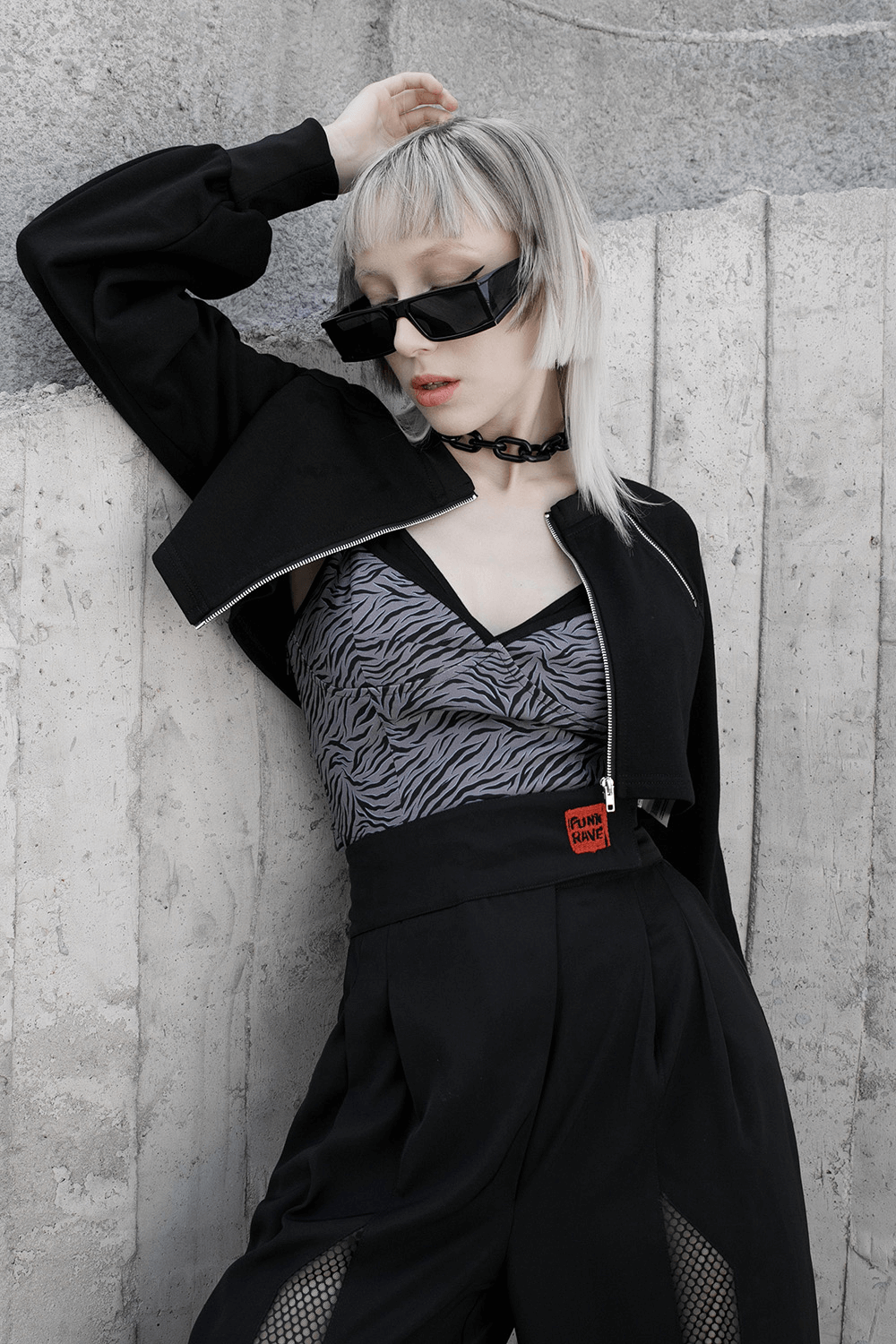 Edgy model in zip-up crop jacket with sunglasses and zebra print top, showcasing punk style and modern fashion.