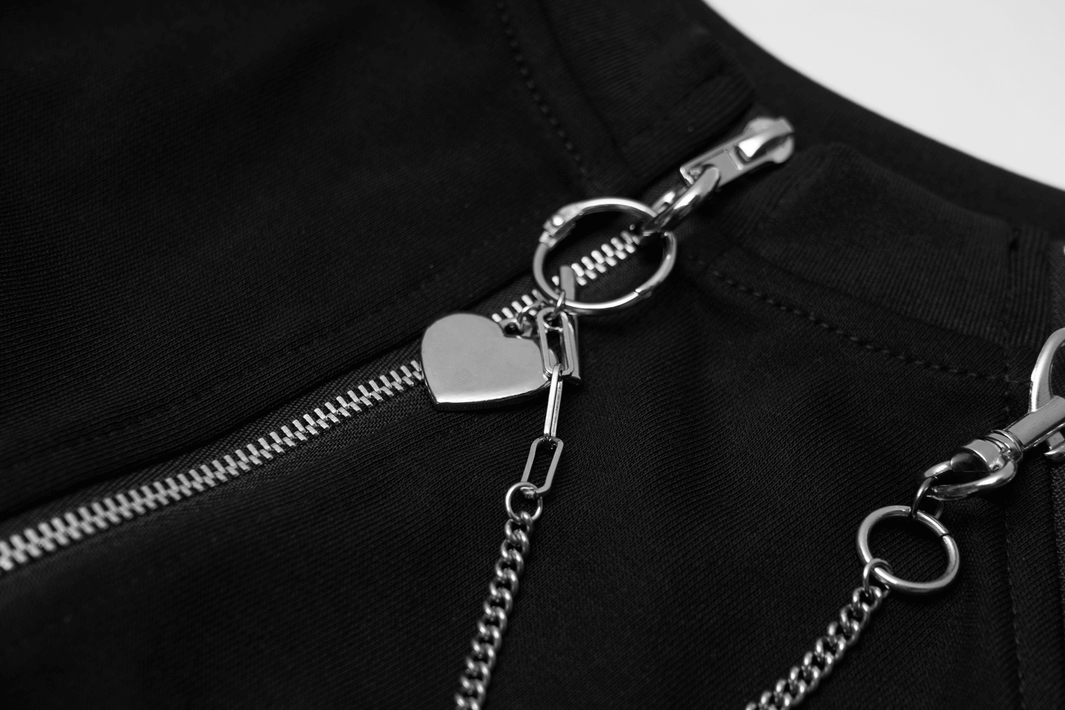 Close-up of a black zip-up crop jacket featuring heart-shaped chain detail and metal zipper.