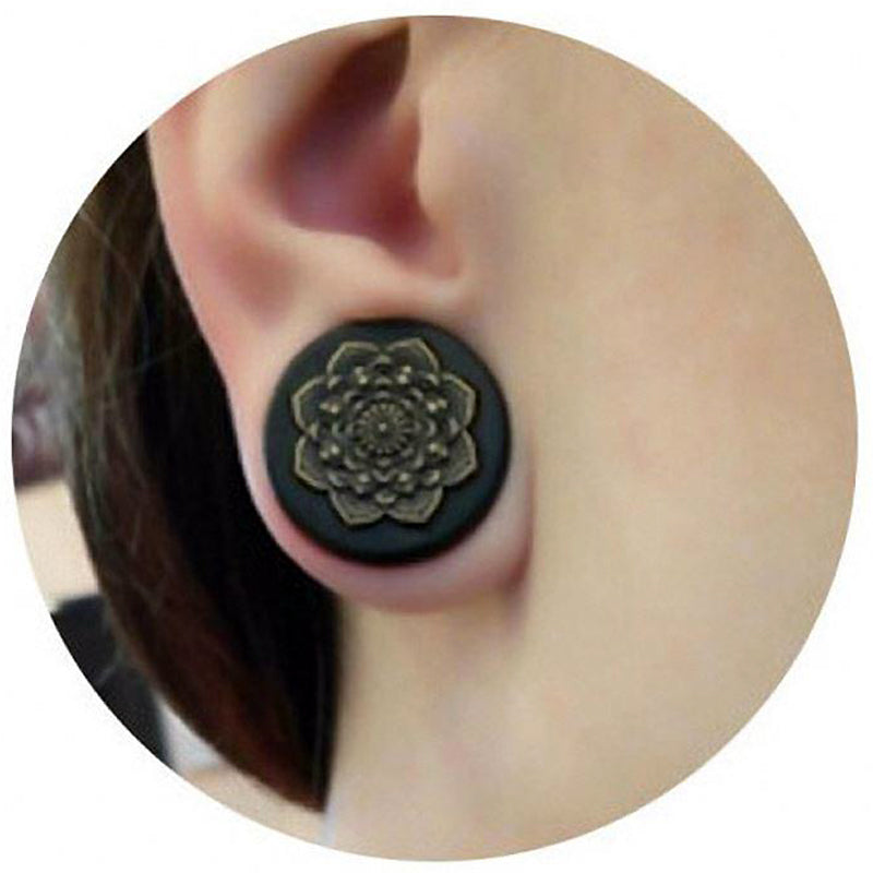 Close-up of a person wearing bamboo wood ear plugs with a carved mandala design, perfect for stretching earlobes.